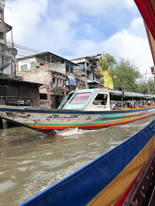 在Khlong Damnoen Saduak运河附近游览时，一艘带篷的木船载着穿着安全夹克的游客，游船行驶在通往Tha Chin和Mae Klong河的水路上